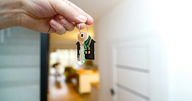 Klucze do nowego mieszkania w dłoni przy drzwiach wejściowych – koszty zakupu mieszkania